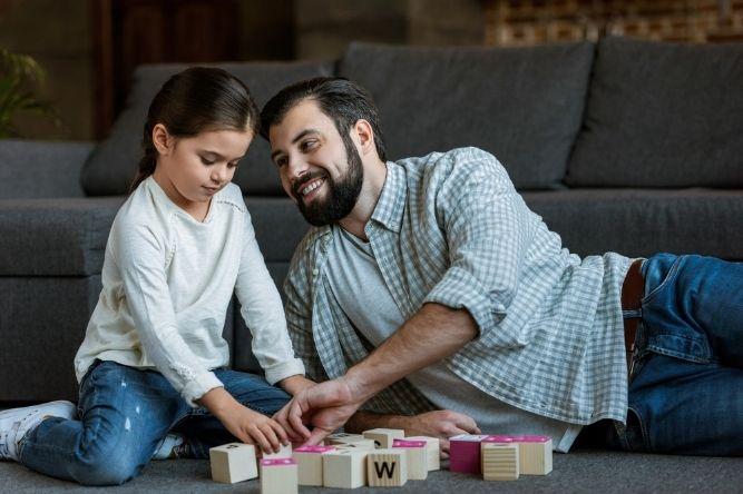Cheerful father with daughter making words by cubes with letters at home 